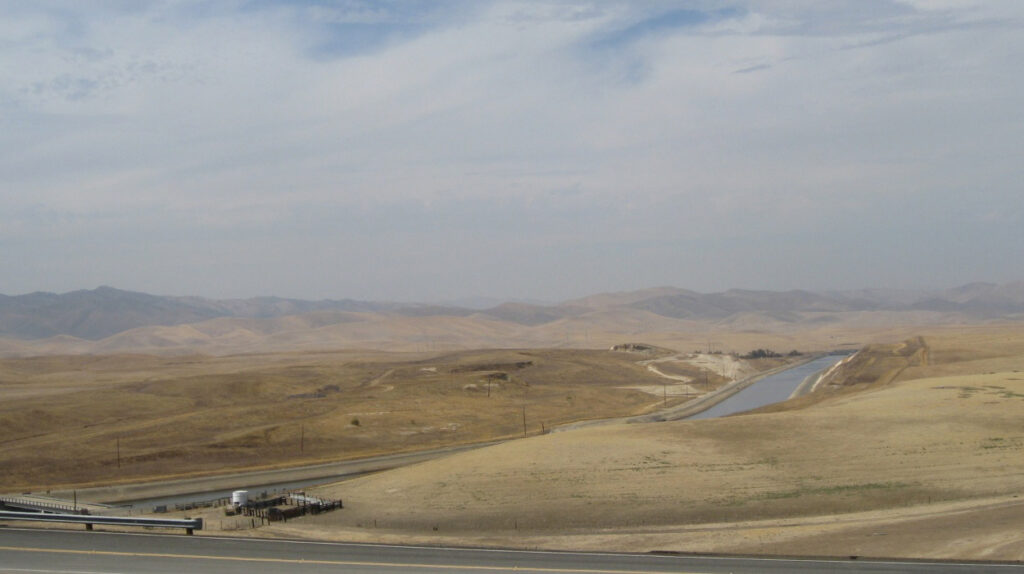 Photograph of concrete aqueduct winding through parched hills. Fallowed agricultural fields surround the route of the California Aqueduct in the western San Joaquin Valley. Credit: Don Barrett via Flickr