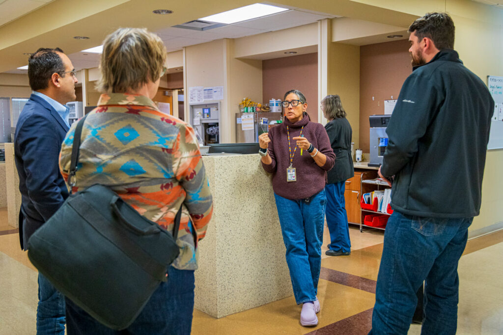 A group of people in conversation, one of them wearing scrubs and a lanyard, inside the Northern Inyo Hospital.